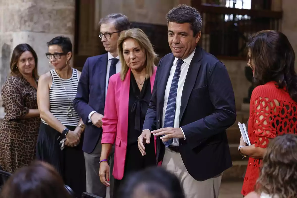 Grupo de personas vestidas de manera formal conversando en un evento en interiores