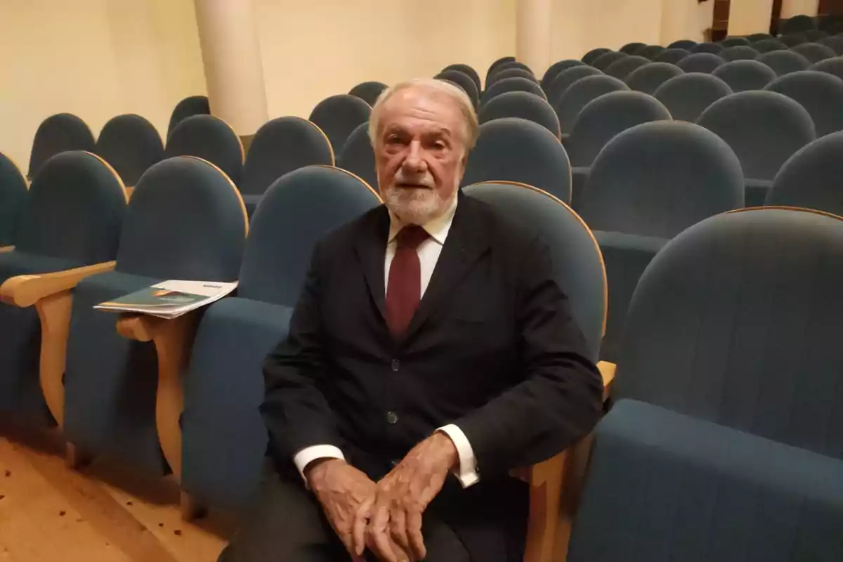 Hombre mayor con barba y traje oscuro sentado en una butaca de un auditorio vacío