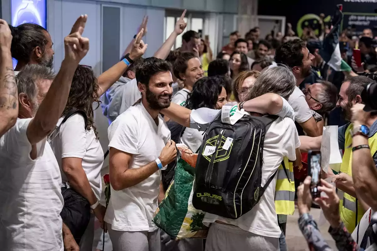 Grupo de personas celebrando y abrazándose en un aeropuerto con expresiones de alegría y brazos levantados