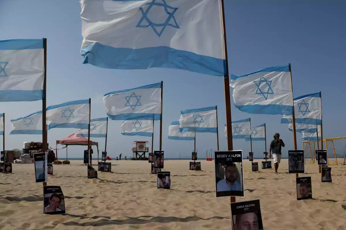 Banderas de Israel ondean en la playa junto a fotografías de personas colocadas en la arena Banderas de Israel ondean en la playa junto a fotografías de personas colocadas en la arena