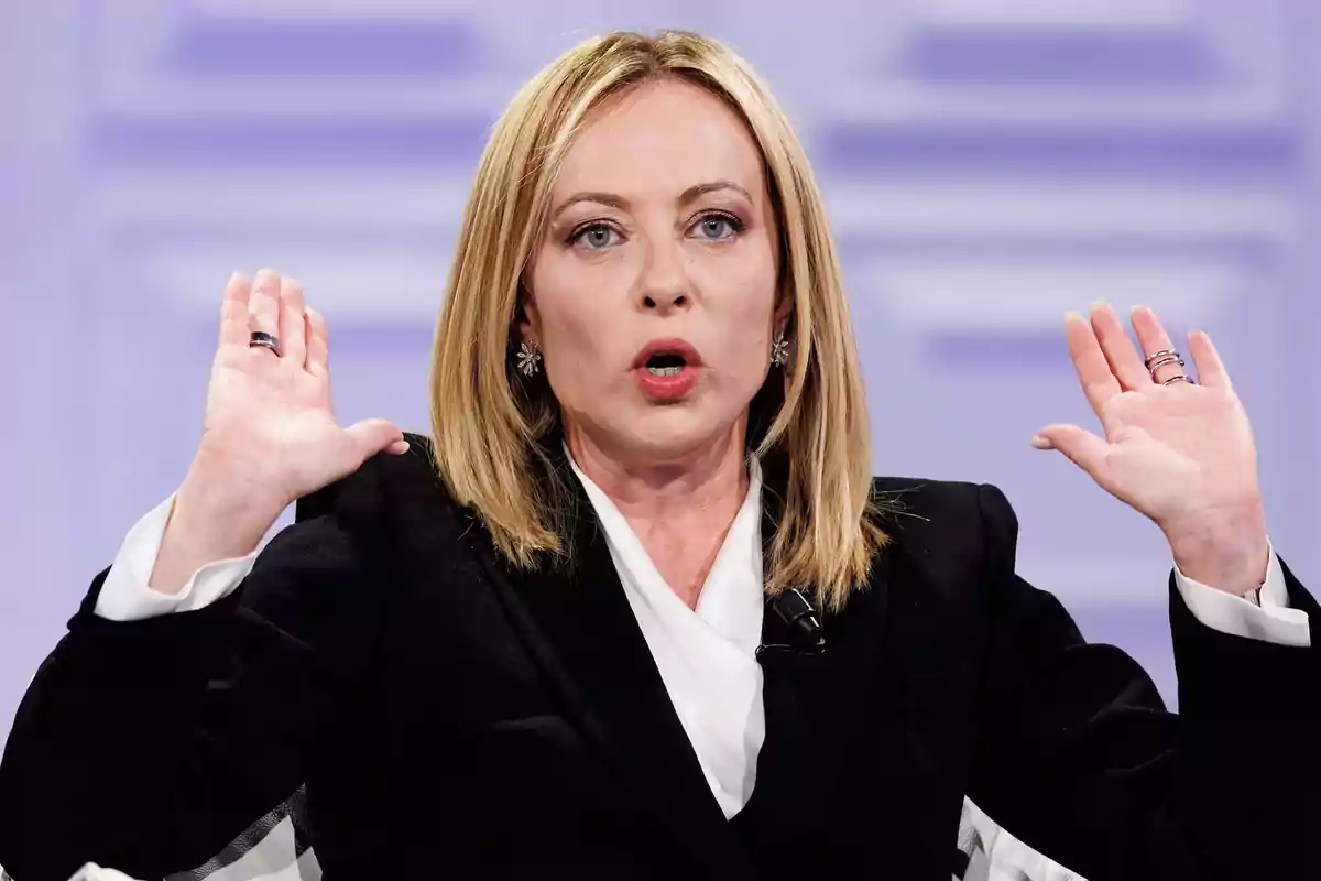 Mujer de cabello rubio y liso con las manos levantadas y expresión seria durante una conversación en un entorno formal