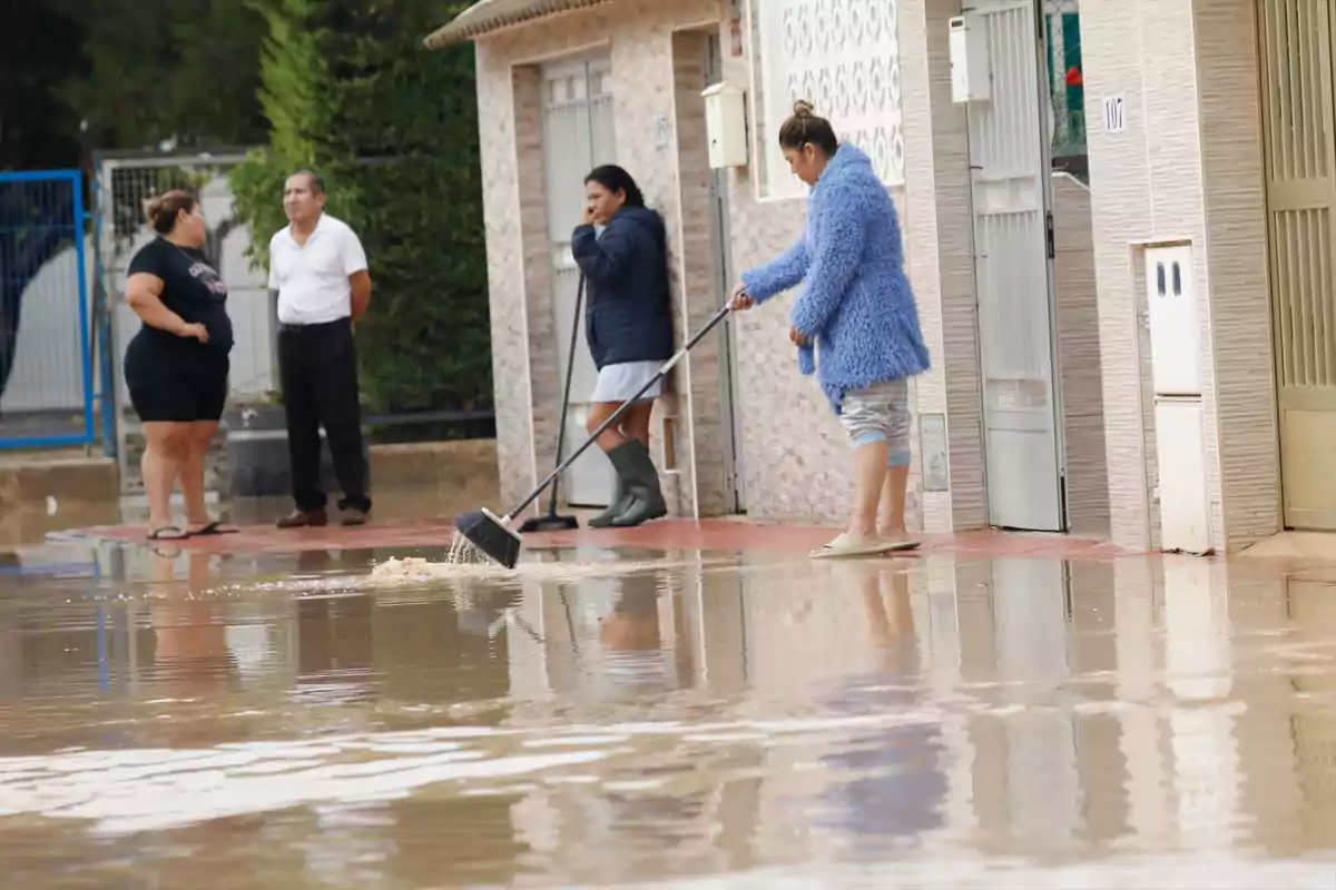 Varias personas intentan limpiar el agua acumulada frente a sus casas tras una inundación en una zona residencial. Varias personas intentan limpiar el agua acumulada frente a sus casas tras una inundación en una zona residencial.