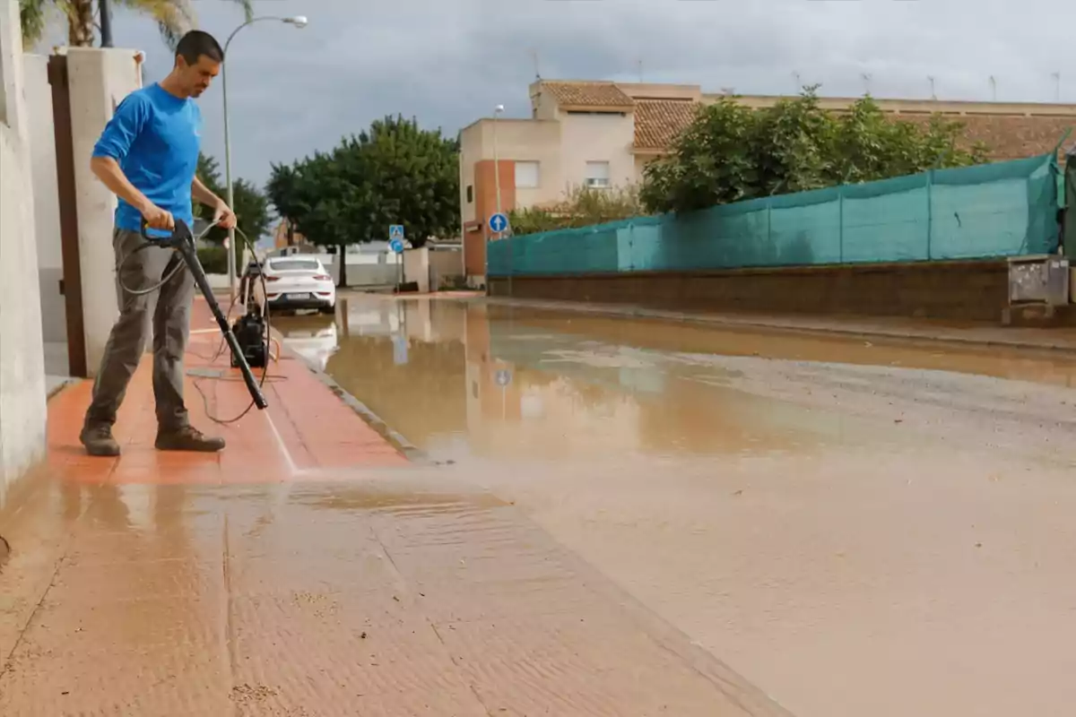 Hombre limpiando una acera con una hidrolavadora tras una inundación en una calle residencial Hombre limpiando una acera con una hidrolavadora tras una inundación en una calle residencial