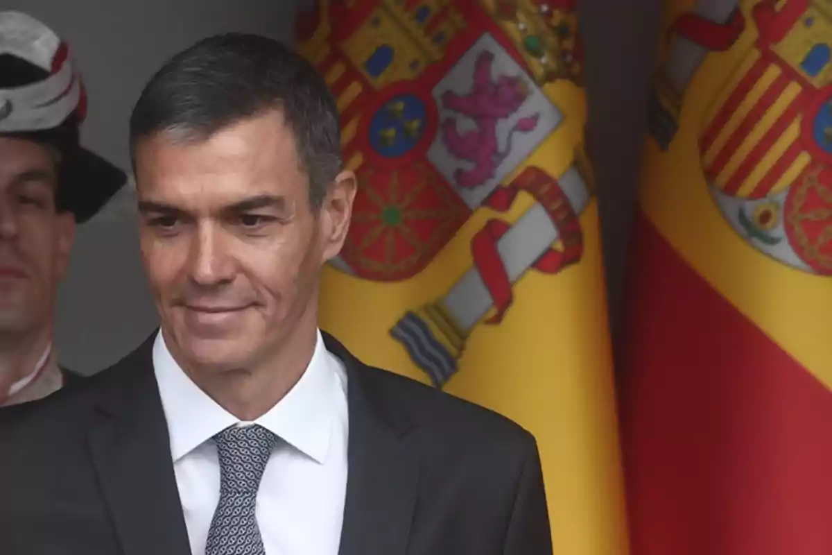 Hombre con traje y corbata frente a banderas de España