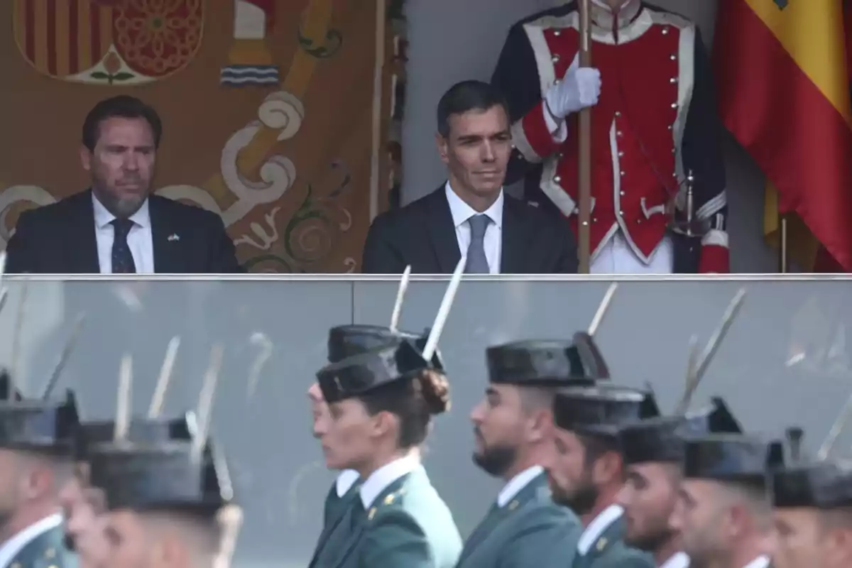 Dos hombres con traje observan un desfile militar donde varios guardias marchan frente a ellos