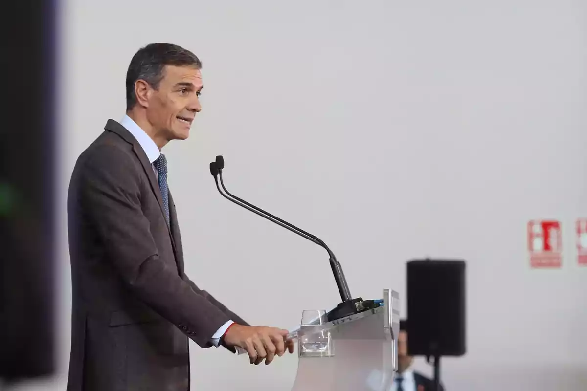 Hombre con traje marrón hablando en un podio con micrófono en un entorno interior