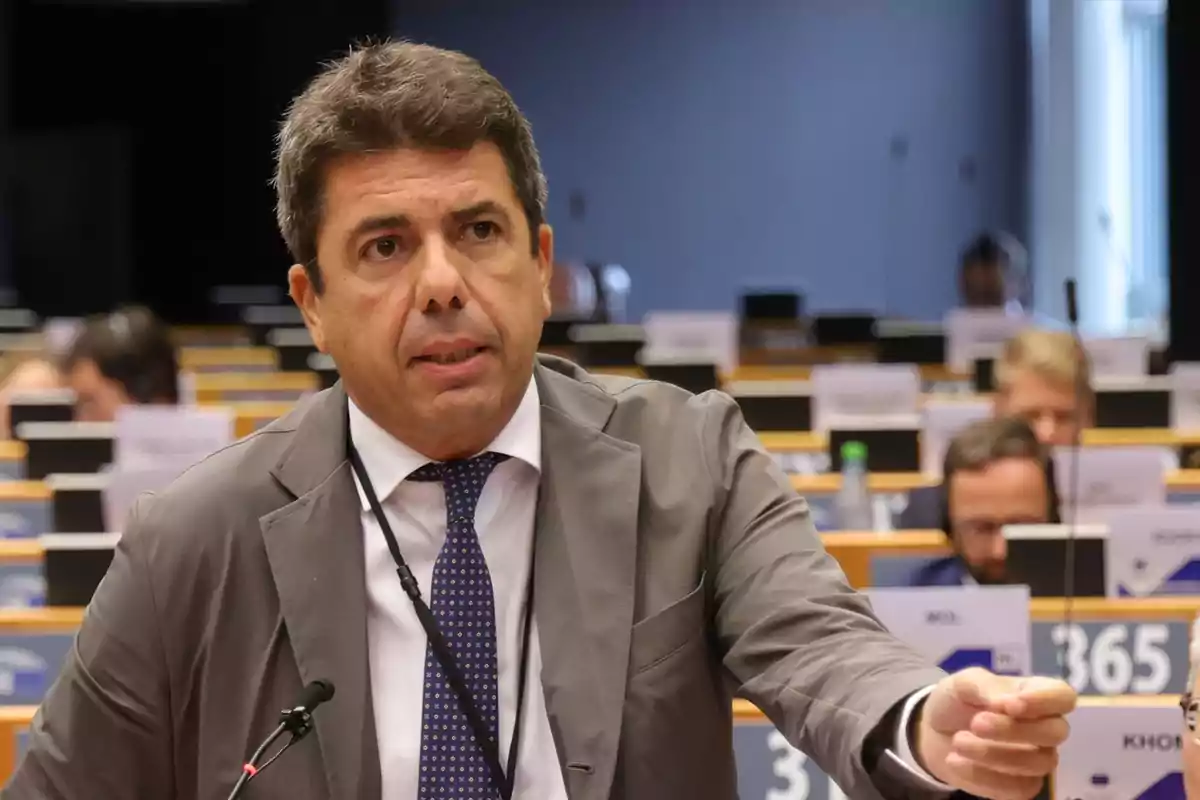 Hombre de cabello corto y canoso hablando en una sala de conferencias con varias personas sentadas al fondo