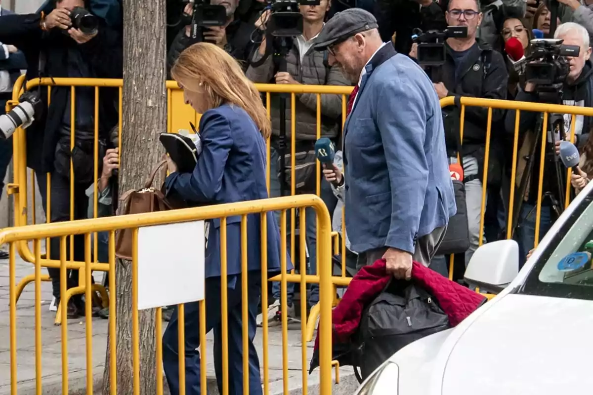 Dos personas caminan junto a una valla amarilla mientras varios periodistas y fotógrafos los observan y toman fotos Dos personas caminan junto a una valla amarilla mientras varios periodistas y fotógrafos los observan y toman fotos