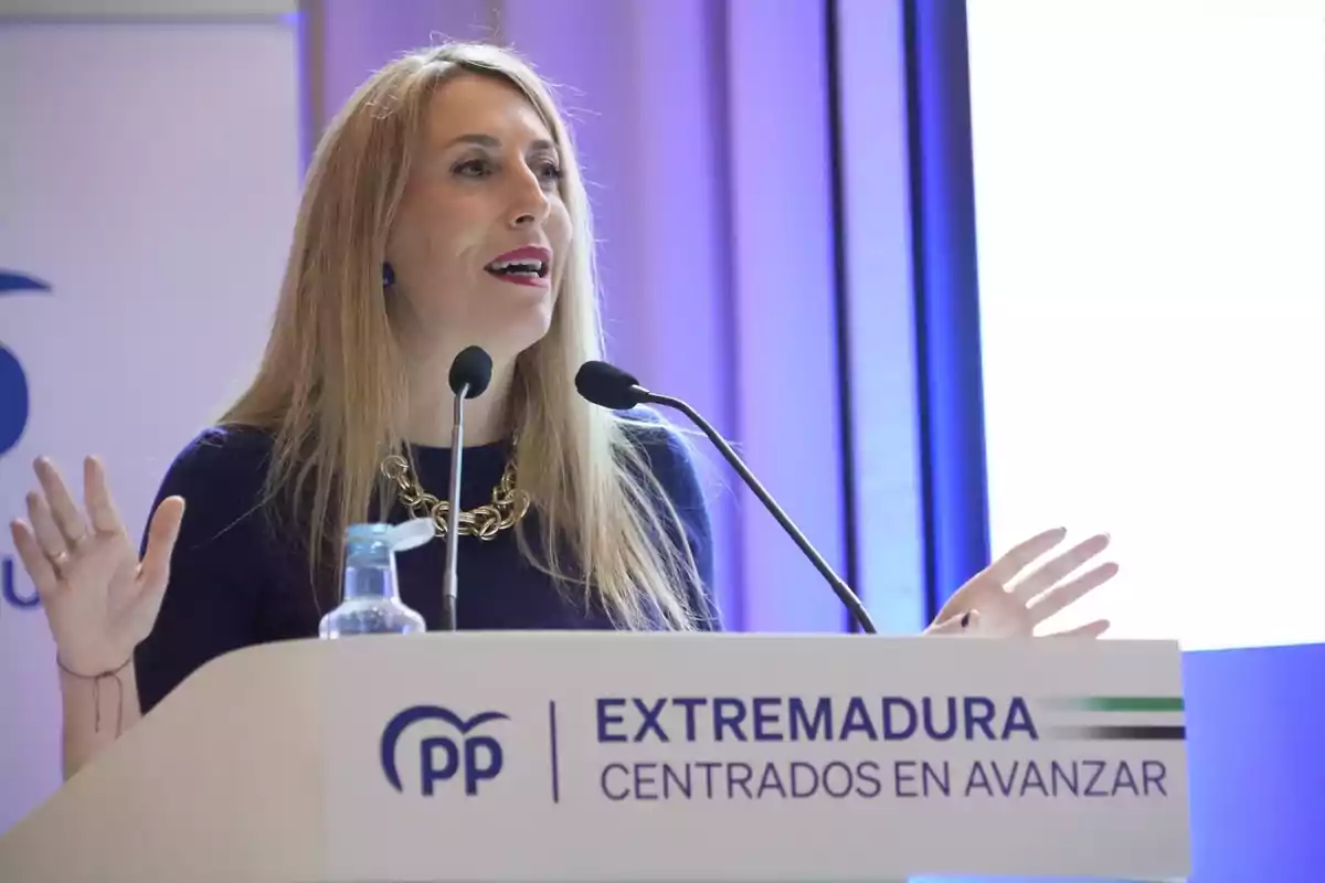 Mujer rubia hablando en un atril con el logo del PP y el texto Extremadura centrados en avanzar