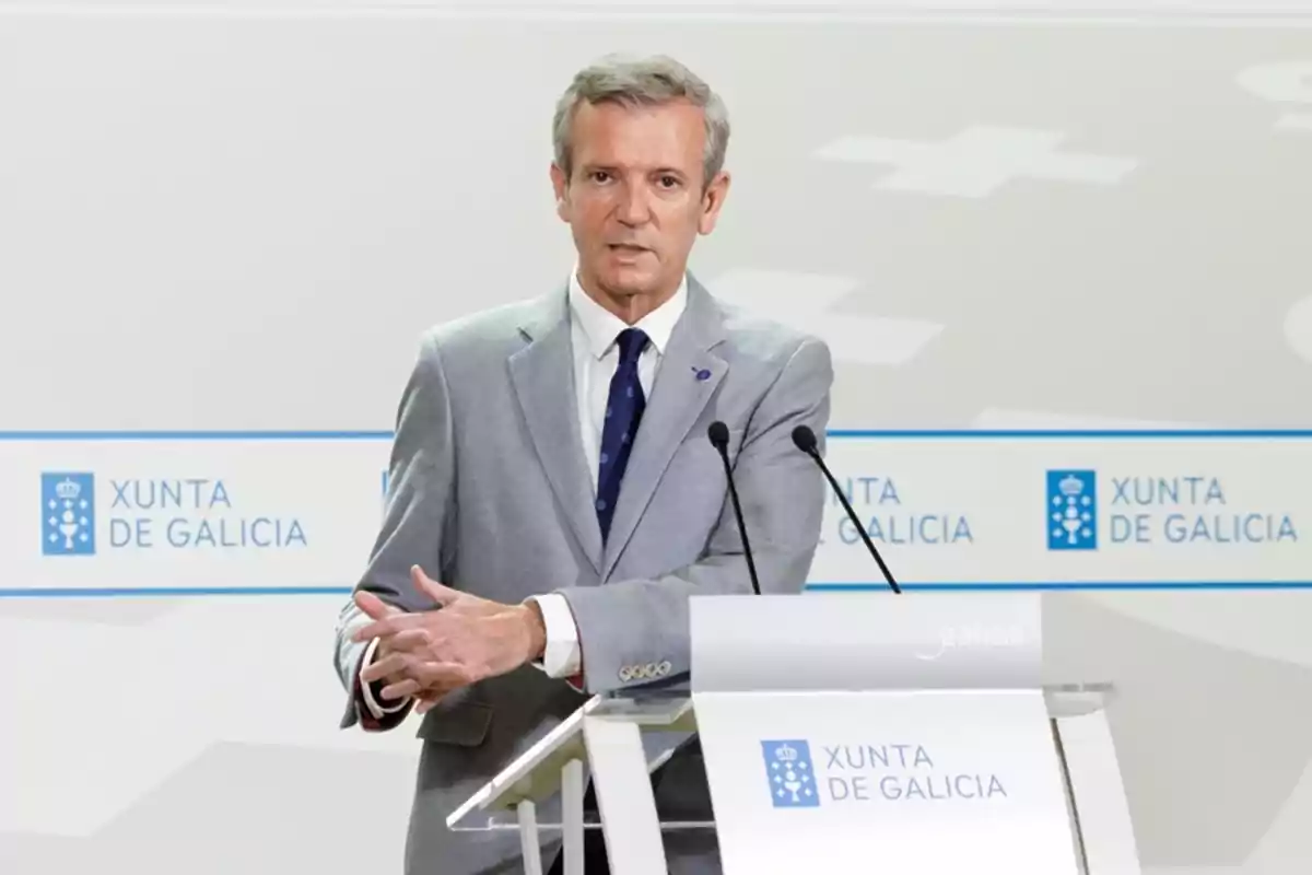 Hombre de cabello canoso con traje gris hablando en un atril con el logo de Xunta de Galicia al fondo