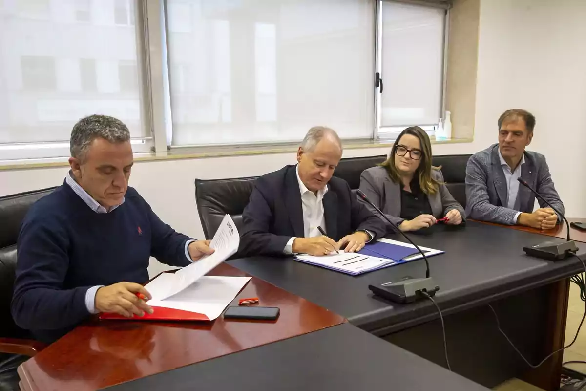 Cuatro personas sentadas en una mesa de reuniones mientras dos de ellas firman documentos oficiales Cuatro personas sentadas en una mesa de reuniones mientras dos de ellas firman documentos oficiales