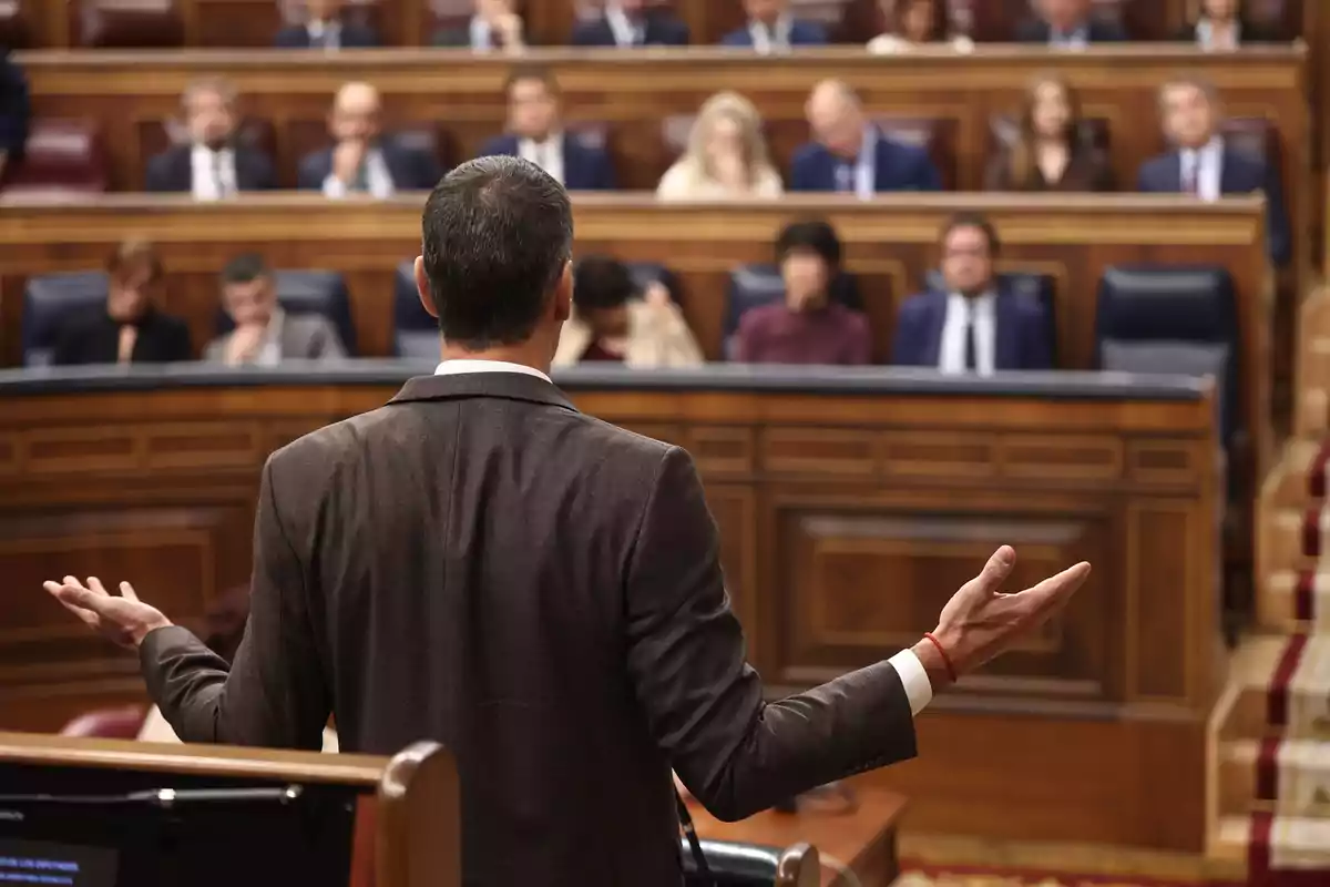 Hombre de espaldas hablando ante un grupo de personas en un parlamento Hombre de espaldas hablando ante un grupo de personas en un parlamento