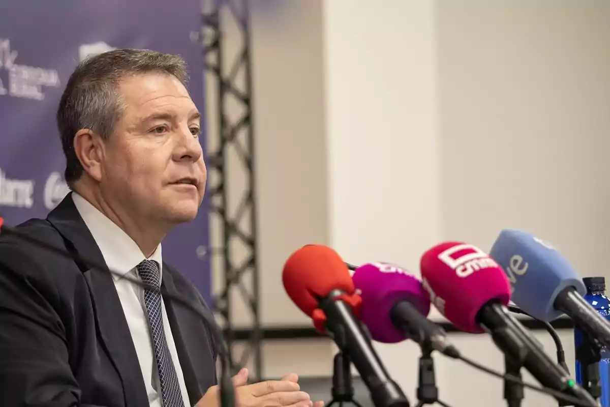 Hombre de traje hablando en una rueda de prensa frente a varios micrófonos de diferentes medios de comunicación Hombre de traje hablando en una rueda de prensa frente a varios micrófonos de diferentes medios de comunicación