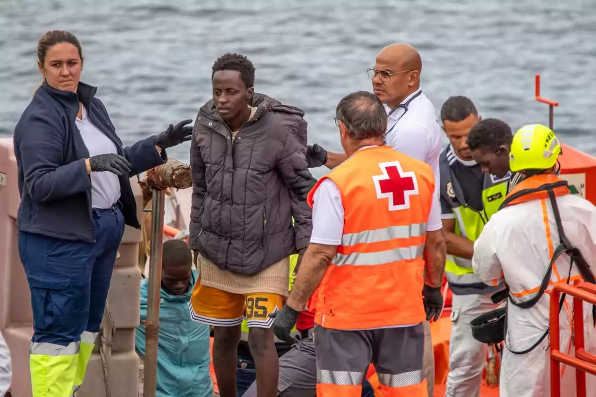 Personal de rescate y asistencia médica ayuda a un grupo de migrantes a desembarcar de una embarcación frente al mar