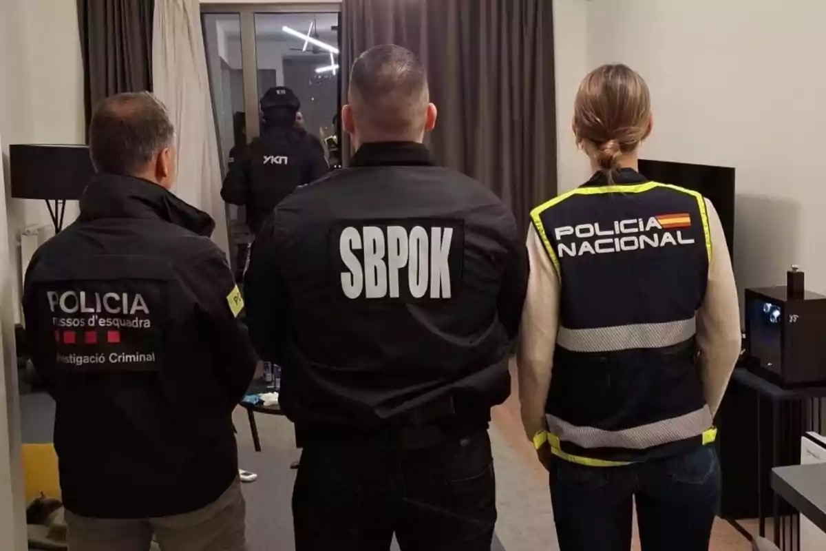Tres agentes de policía de espaldas dentro de una habitación, cada uno con uniforme de diferentes cuerpos policiales