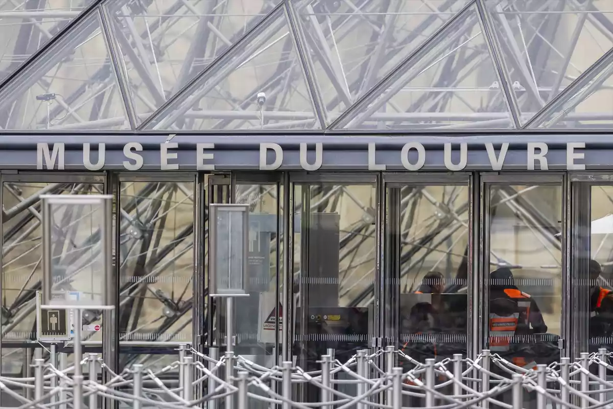 Entrada principal del Museo del Louvre con puertas de vidrio y estructura de pirámide de cristal