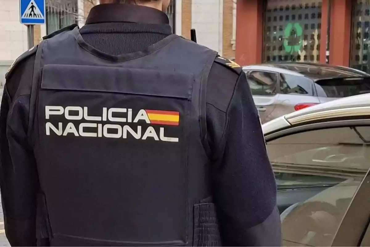 Agente de la Policía Nacional de España de espaldas junto a un coche patrulla en una calle urbana