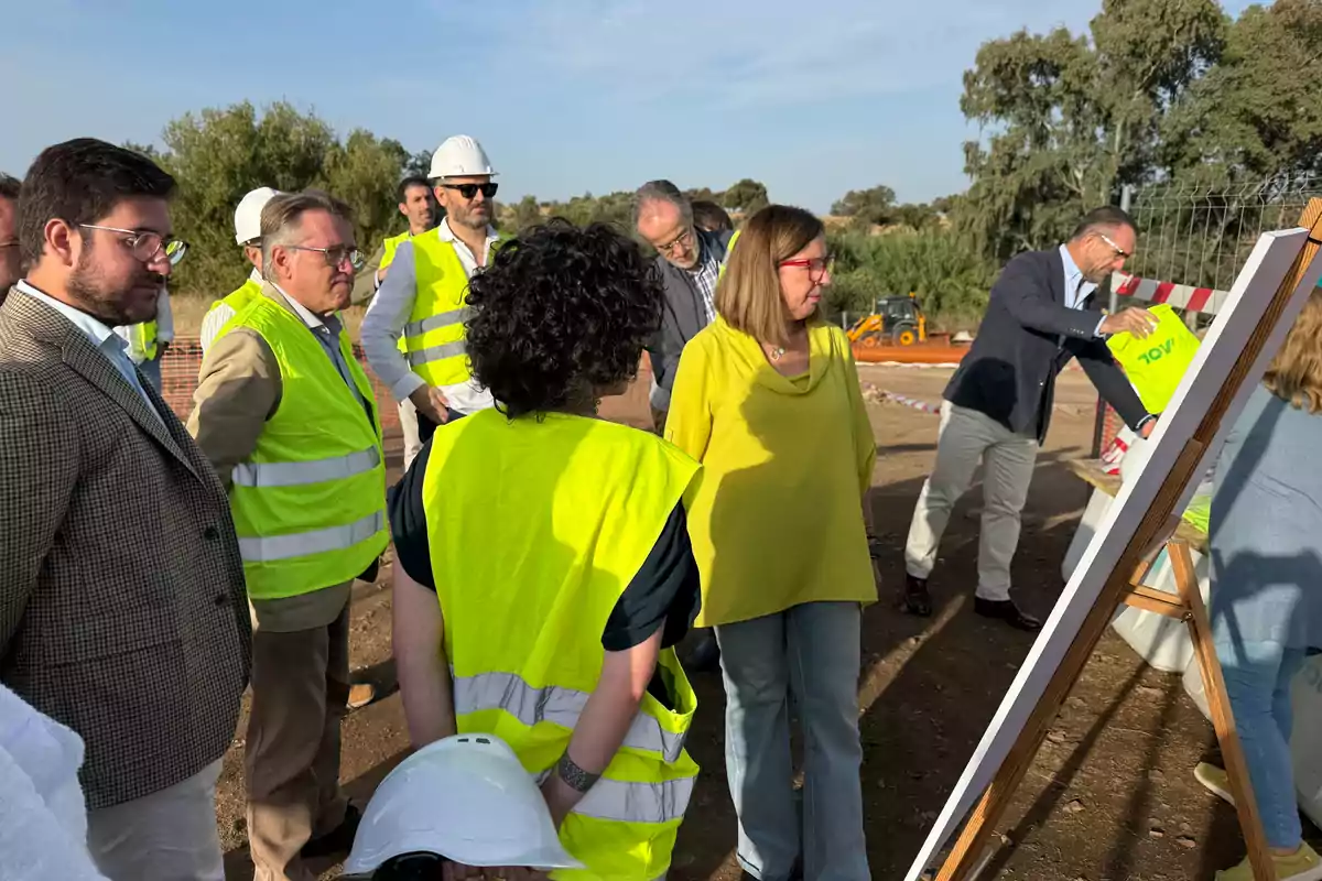 Un grupo de personas con chalecos reflectantes y cascos de seguridad observa un plano en una obra al aire libre