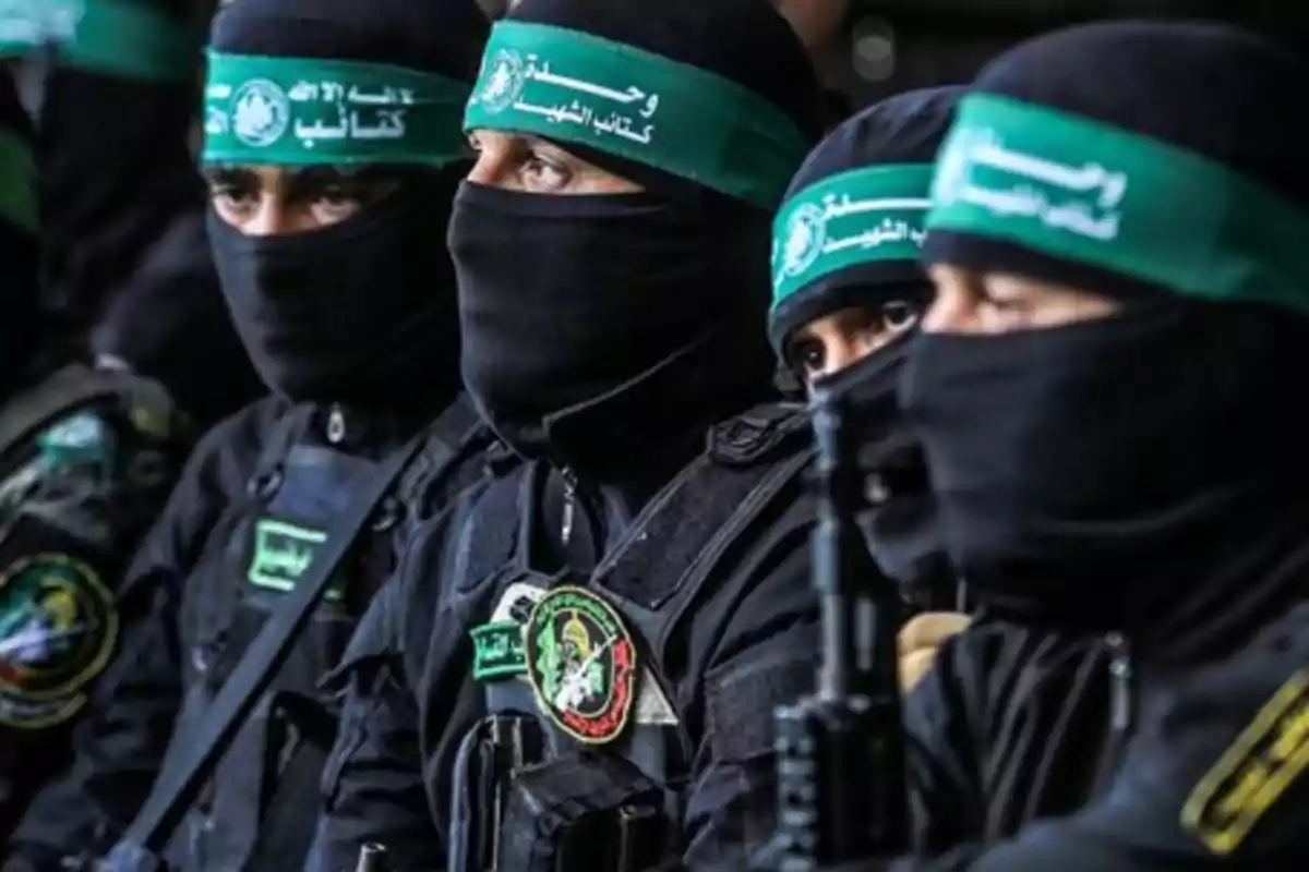 Grupo de personas con uniformes oscuros, pasamontañas y cintas verdes en la cabeza, sentados en fila y mirando hacia el mismo lado Grupo de personas con uniformes oscuros, pasamontañas y cintas verdes en la cabeza, sentados en fila y mirando hacia el mismo lado