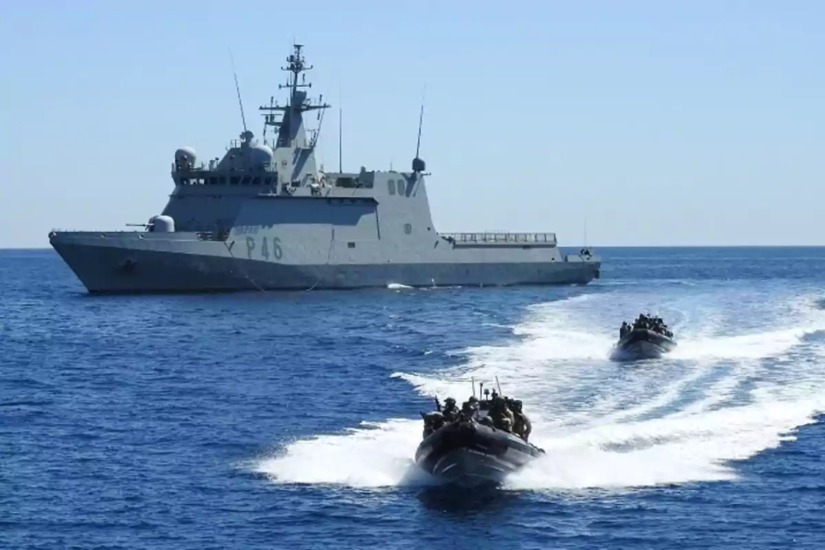 Buque militar navegando en el mar acompañado por dos lanchas rápidas con personal a bordo