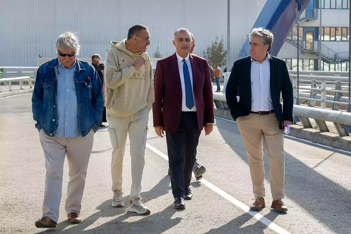 Cuatro hombres caminan juntos por una calle, dos de ellos llevan chaqueta y corbata, uno viste ropa deportiva clara y otro lleva chaqueta de mezclilla y gafas de sol. Cuatro hombres caminan juntos por una calle, dos de ellos llevan chaqueta y corbata, uno viste ropa deportiva clara y otro lleva chaqueta de mezclilla y gafas de sol.