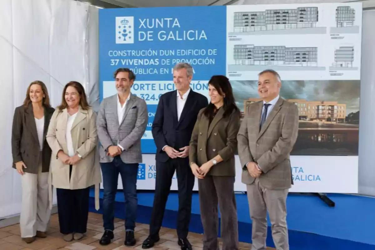 Seis personas posan sonrientes frente a un cartel de la Xunta de Galicia que anuncia la construcción de un edificio de 37 viviendas de promoción pública, con planos y una imagen del proyecto arquitectónico al fondo.