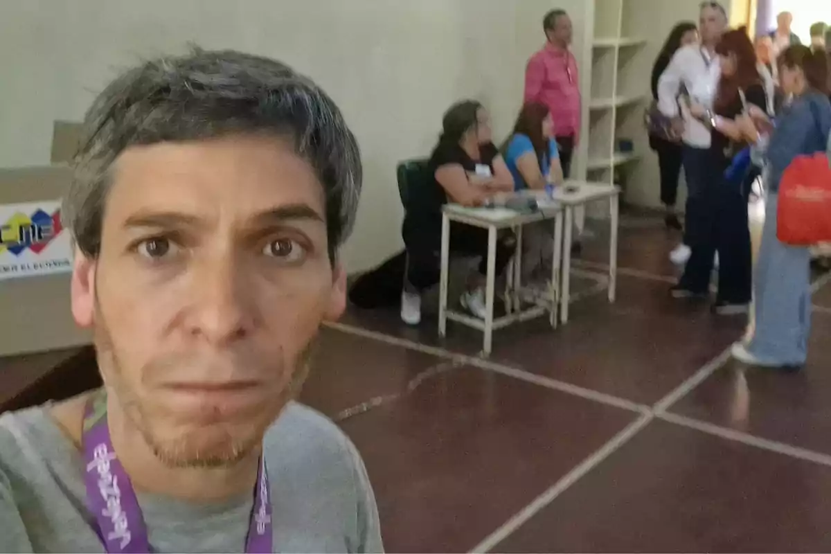 Hombre tomándose una selfie en un centro de votación con varias personas al fondo participando en el proceso electoral. Hombre tomándose una selfie en un centro de votación con varias personas al fondo participando en el proceso electoral.
