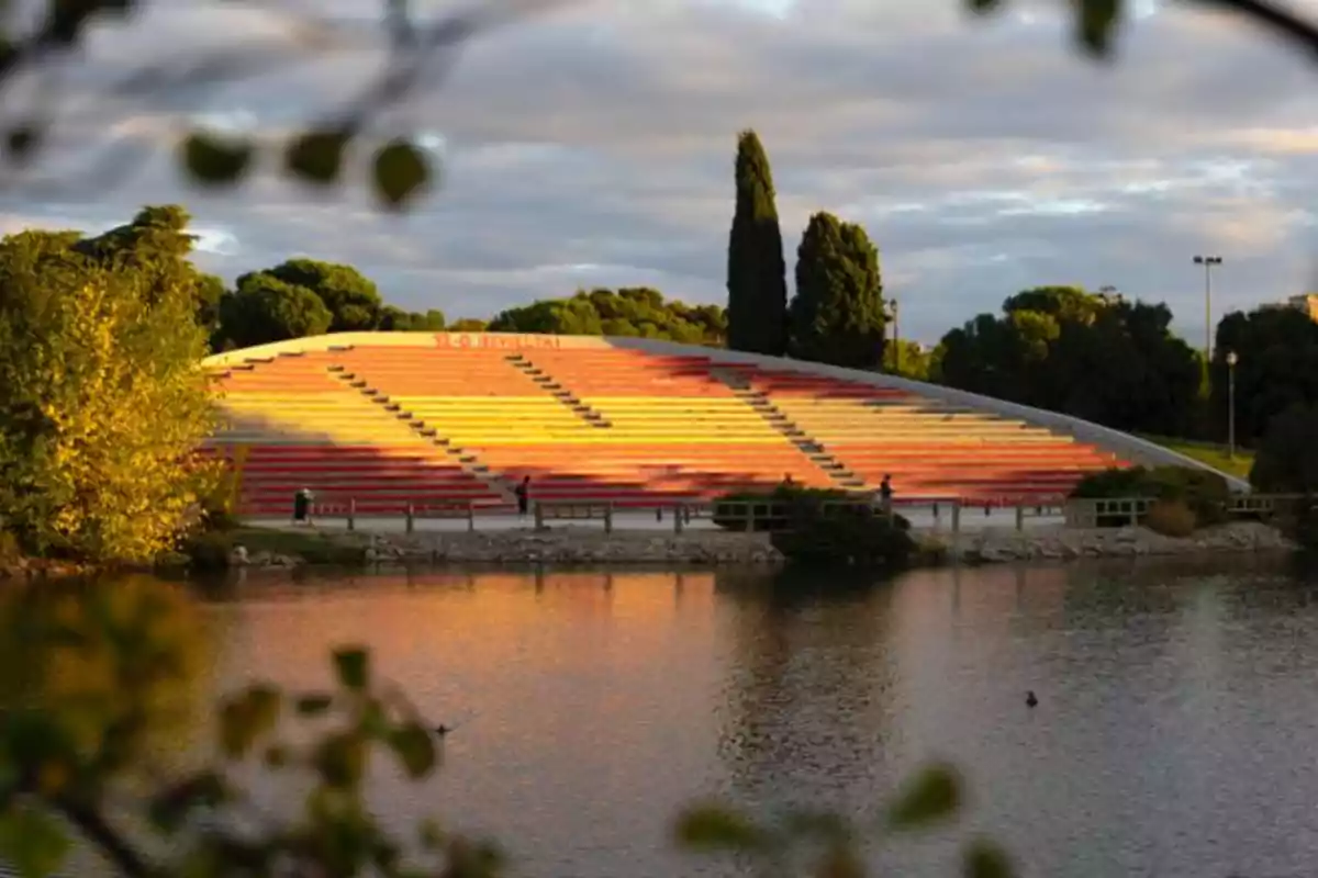Gradas de colores rojo y amarillo reflejadas en un lago rodeado de árboles al atardecer Gradas de colores rojo y amarillo reflejadas en un lago rodeado de árboles al atardecer
