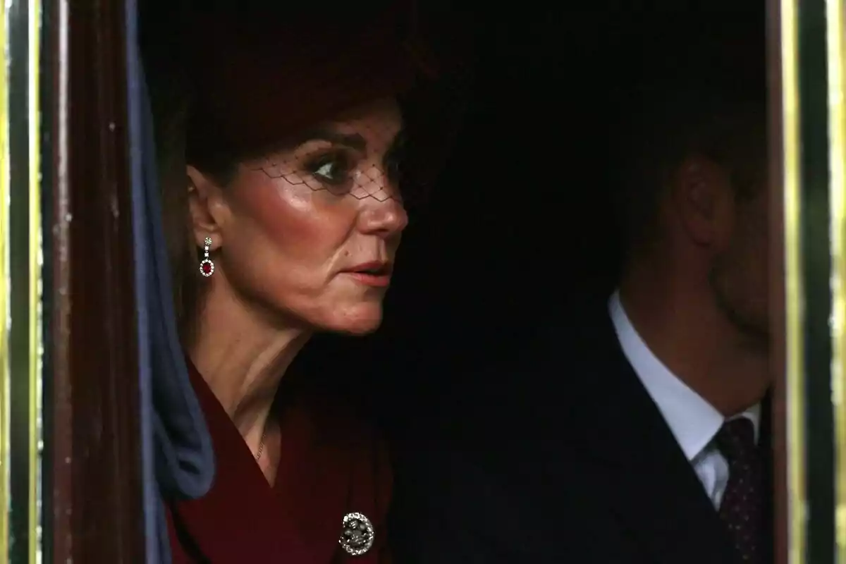 Mujer elegantemente vestida con sombrero y velo oscuro sentada junto a un hombre en un ambiente tenue