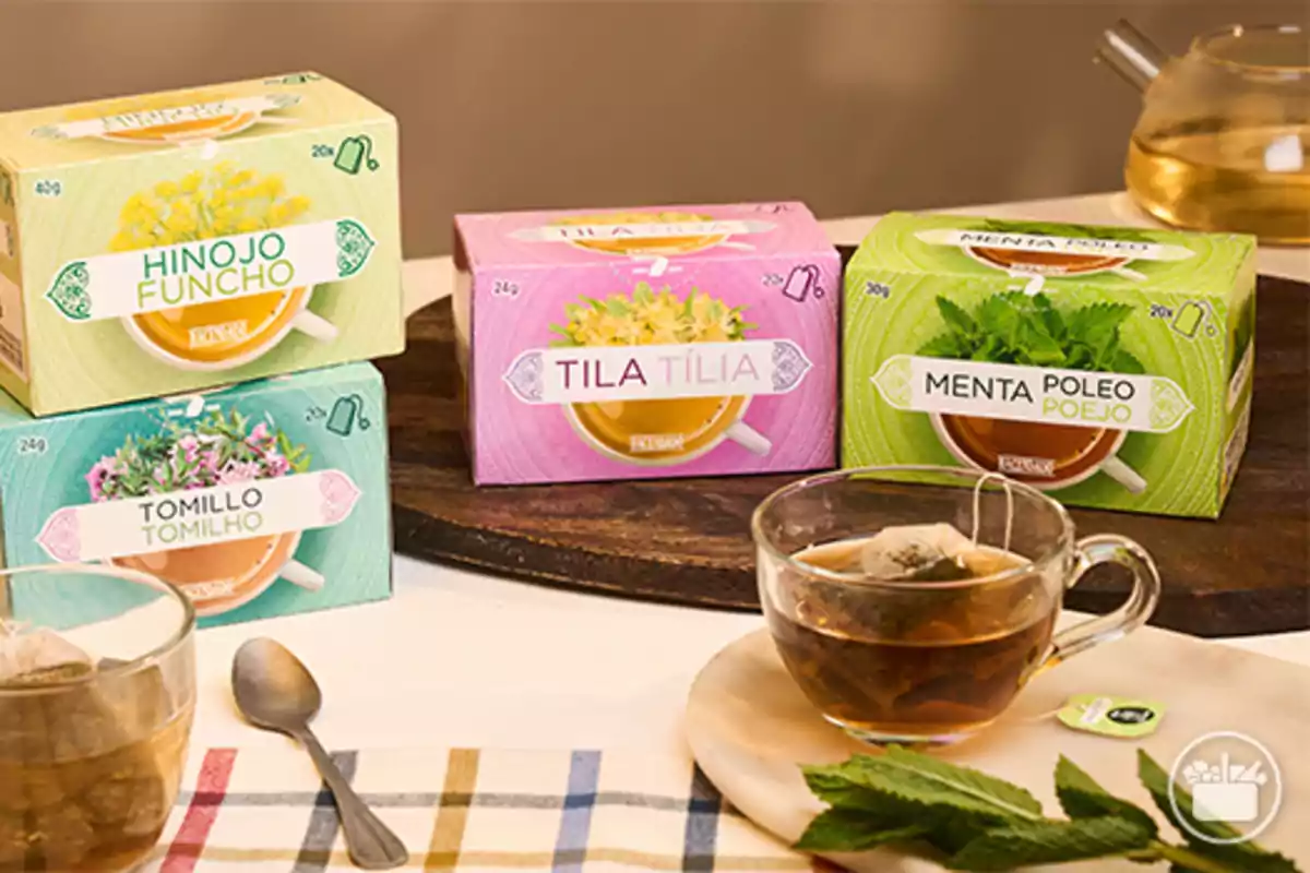 Cajas de infusiones de hierbas variadas junto a una taza de té y una tetera sobre una mesa