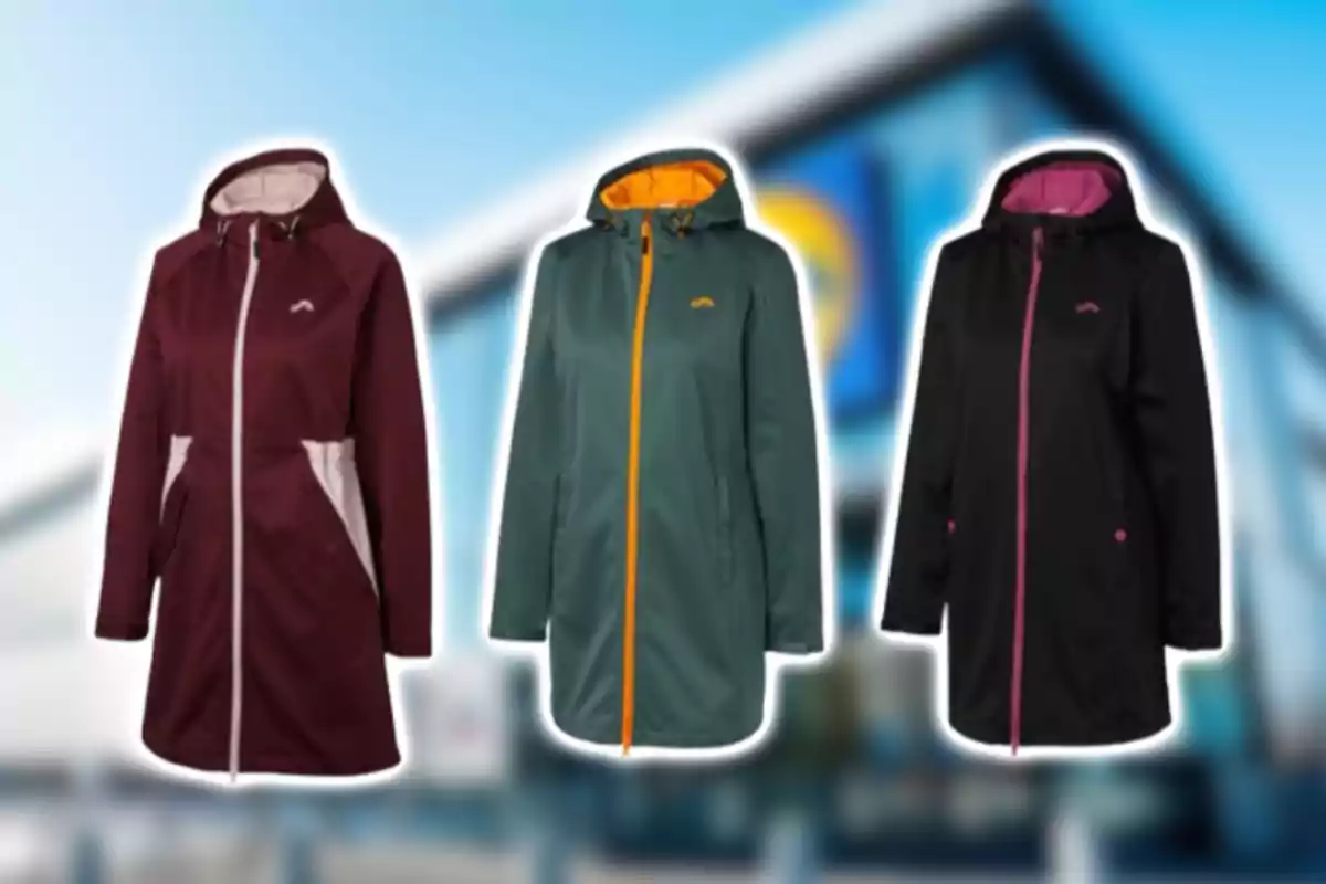 Tres chaquetas impermeables de mujer en colores vino, verde y negro con detalles en contraste, sobre un fondo desenfocado de una tienda