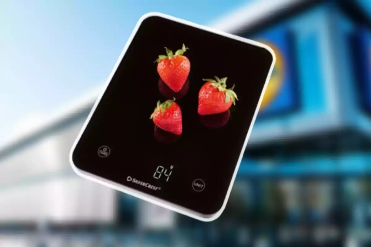 Báscula digital negra con tres fresas encima mostrando un peso de 84 gramos frente a un fondo desenfocado de un edificio.