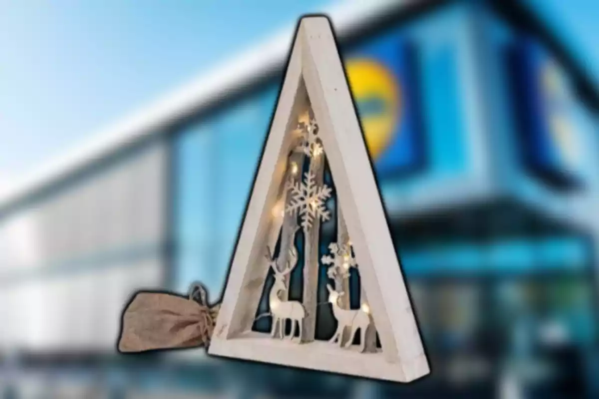 Adorno navideño en forma de triángulo de madera con luces y figuras de renos y copos de nieve frente a una tienda desenfocada