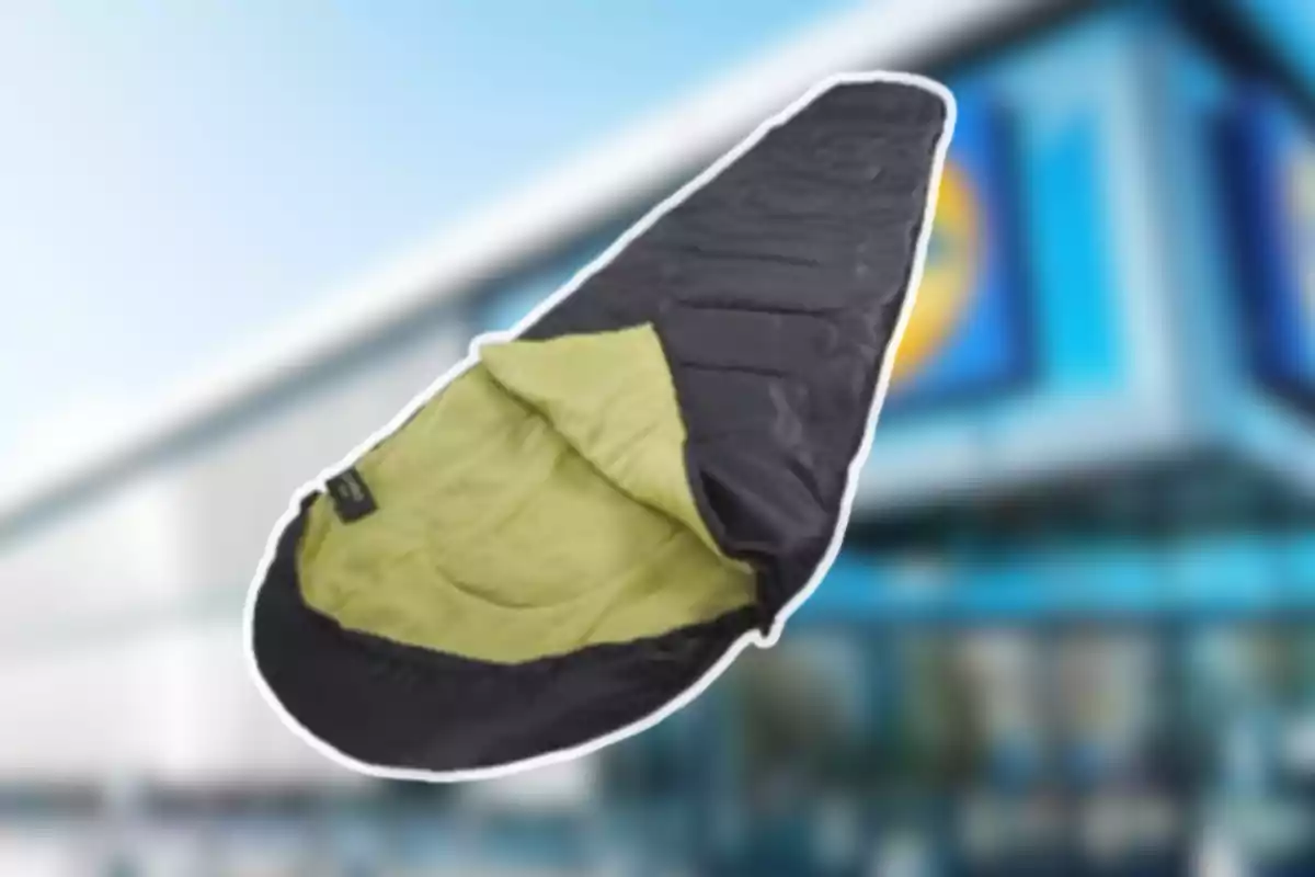 Saco de dormir negro con interior verde claro frente a un edificio desenfocado