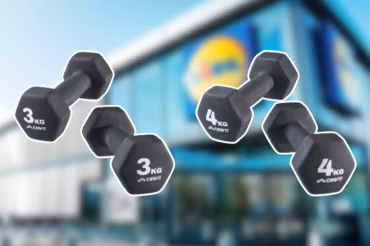 Cuatro mancuernas negras de 3 y 4 kilos flotando frente a una tienda con el logo de Lidl desenfocado al fondo