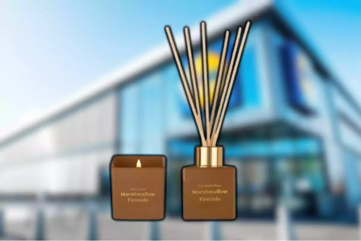 Vela aromática y difusor de varillas color marrón con la etiqueta Marshmallow Fireside frente a un edificio moderno desenfocado