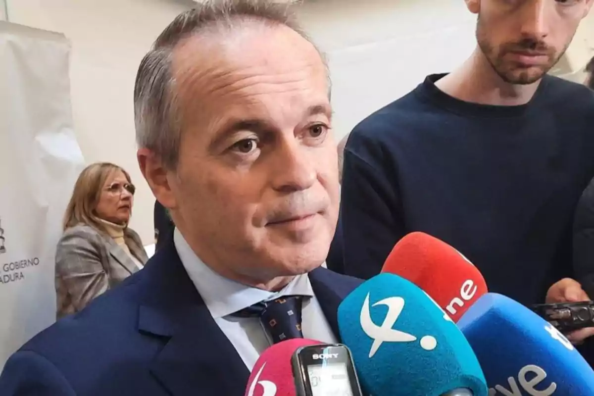 Hombre de traje hablando frente a varios micrófonos de diferentes medios de comunicación mientras es entrevistado