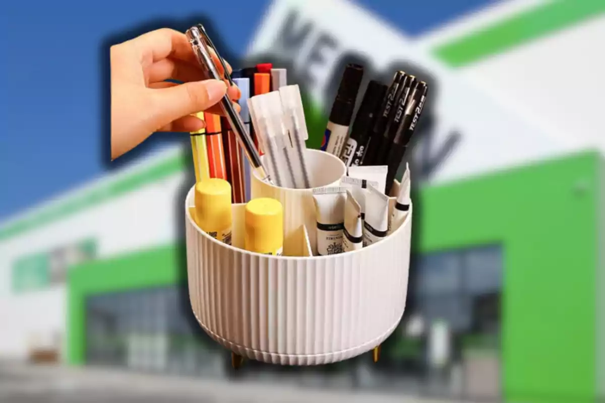 Una mano toma un bolígrafo de un organizador blanco lleno de útiles de oficina con un edificio desenfocado al fondo