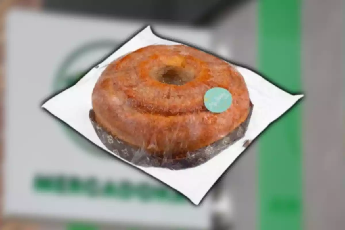 Pastel tipo rosca envuelto en plástico sobre un fondo borroso con colores verde y gris