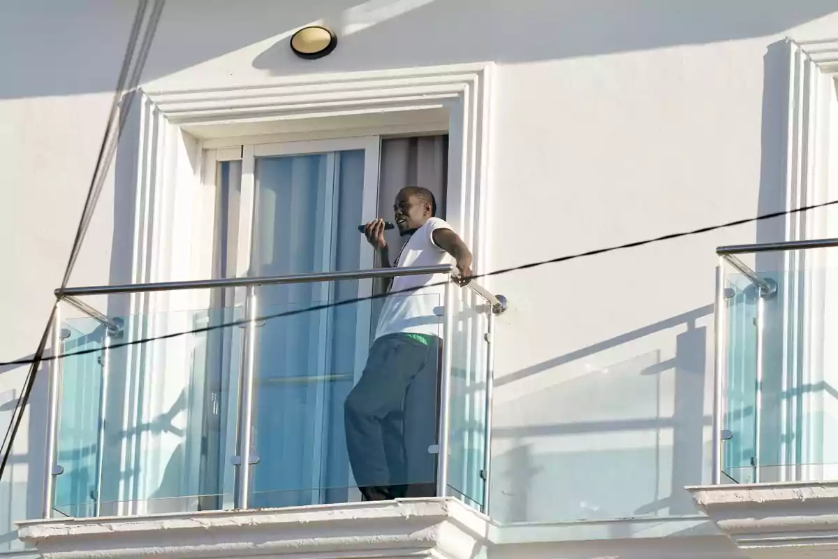 Hombre de pie en un balcón de cristal hablando por teléfono frente a una pared blanca Hombre de pie en un balcón de cristal hablando por teléfono frente a una pared blanca