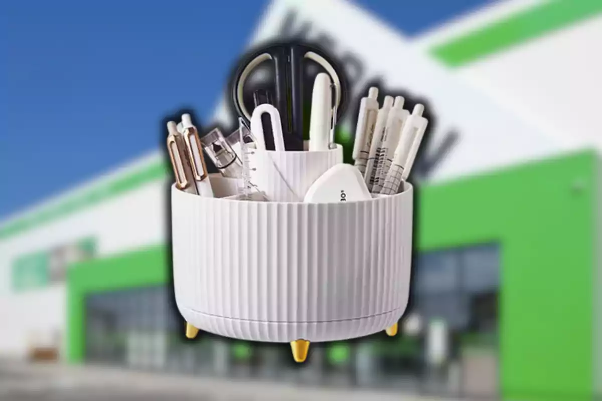 Un organizador blanco con varios artículos de papelería como tijeras, bolígrafos y reglas al frente de un edificio con detalles verdes y blancos.