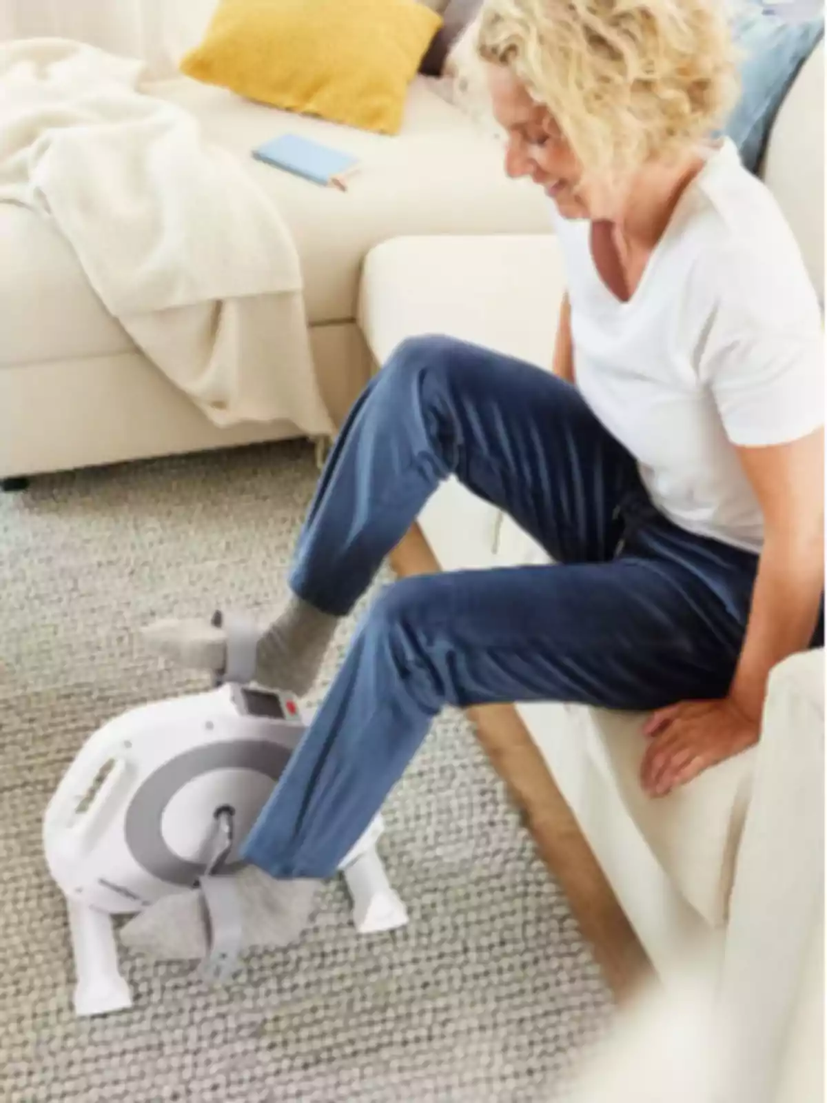 Mujer sentada en un sofá usando una bicicleta estática pequeña sobre una alfombra en una sala de estar