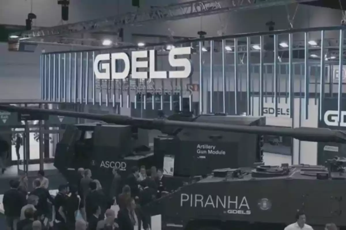 Exhibición de vehículos blindados y artillería en un evento de la empresa GDELS con varias personas observando los equipos.