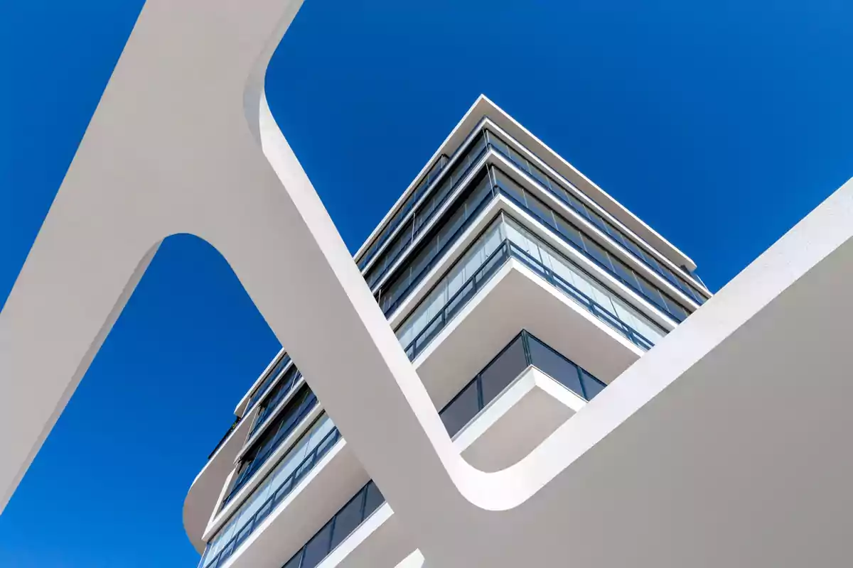 Edificio moderno de líneas blancas y ventanales de vidrio visto desde un ángulo bajo con cielo azul despejado