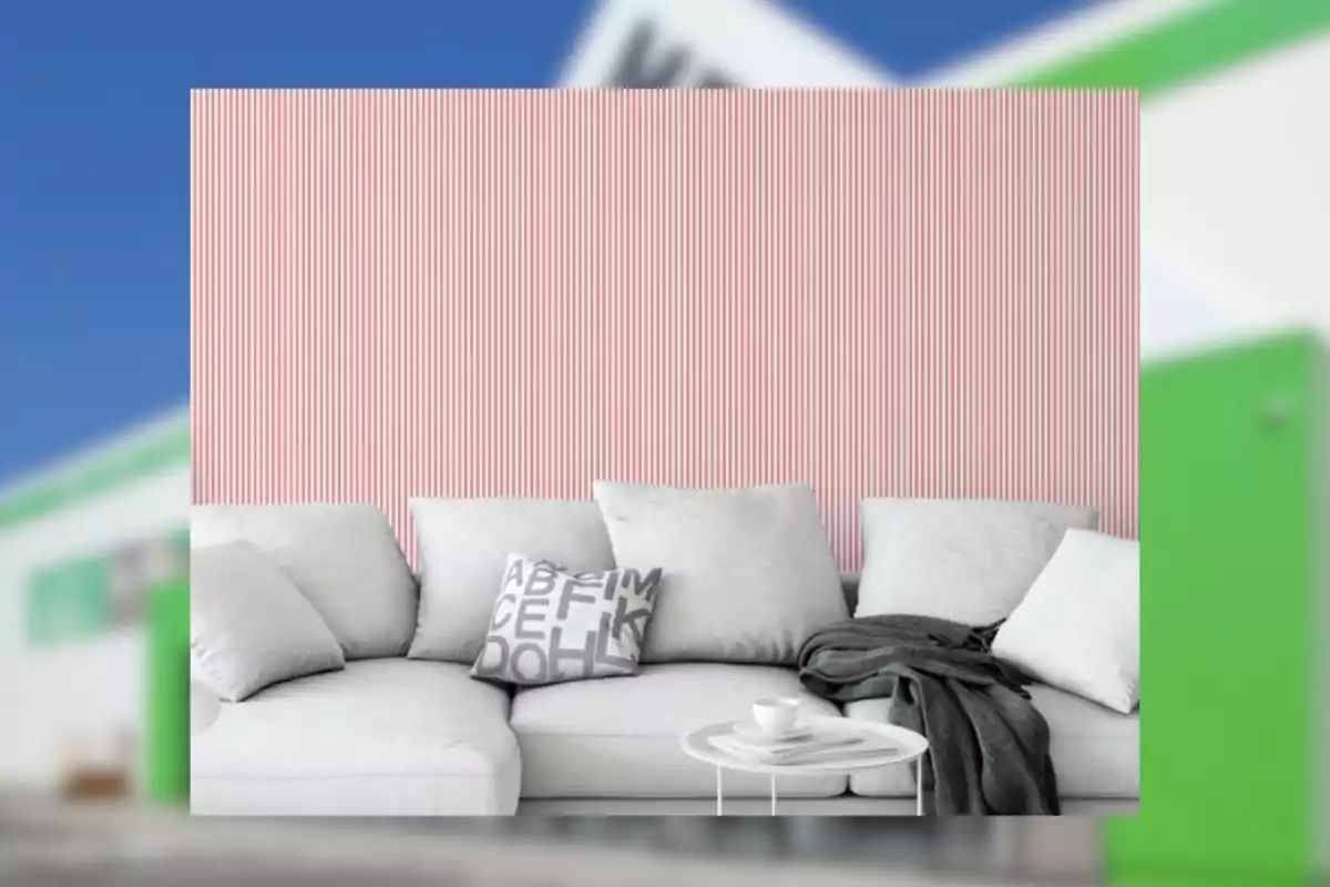 Sofá blanco con cojines y manta gris frente a una pared con rayas verticales rosas y blancas, junto a una mesa pequeña con una taza y un plato.