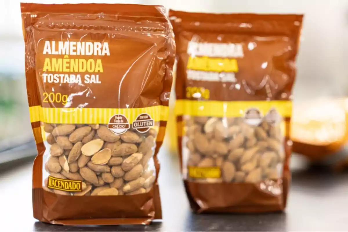 Dos bolsas de almendras tostadas con sal de la marca Hacendado sobre una superficie, una en primer plano y otra desenfocada al fondo