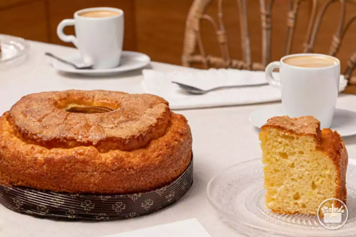 Bizcocho esponjoso con azúcar por encima acompañado de dos tazas de café sobre una mesa con mantel blanco