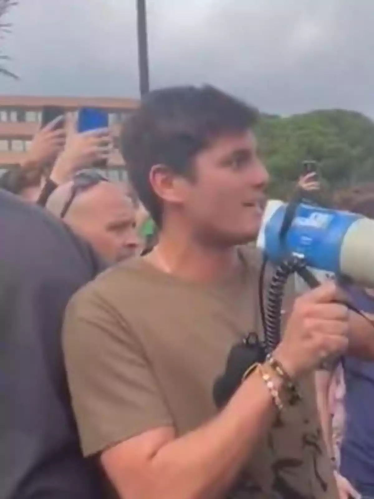 Joven sosteniendo un megáfono en medio de una multitud al aire libre Joven sosteniendo un megáfono en medio de una multitud al aire libre
