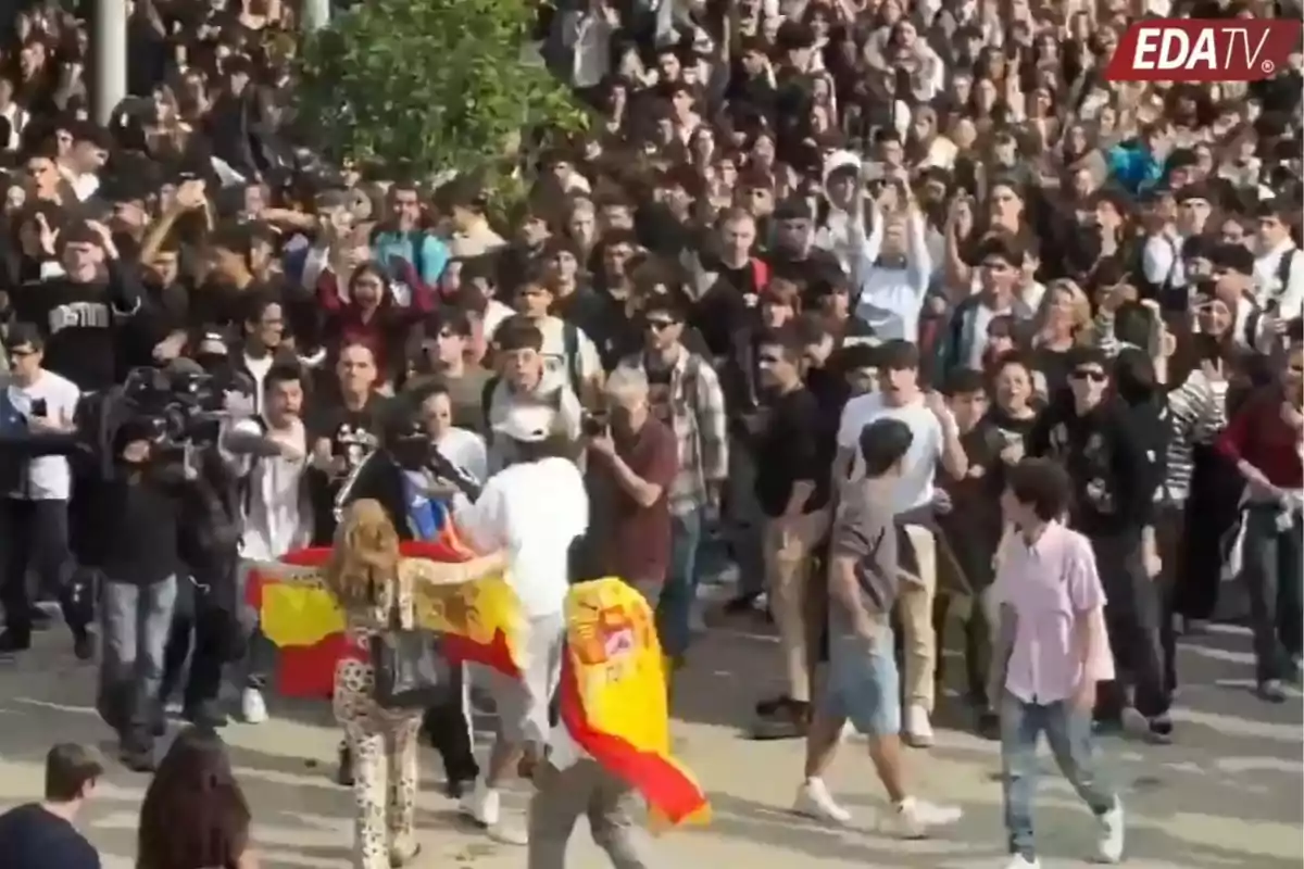 Una multitud de personas reunidas al aire libre mientras algunas ondean banderas de España y varias cámaras graban la escena