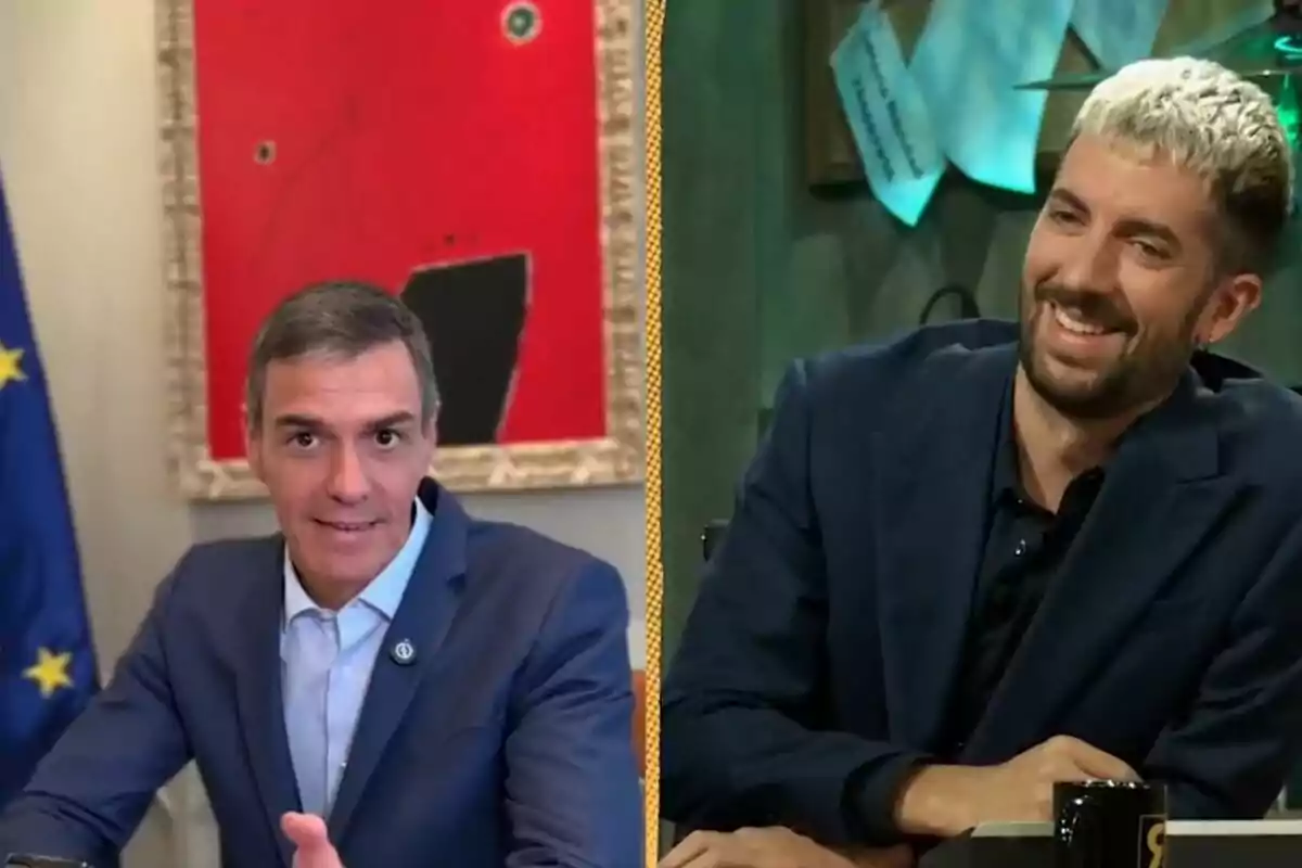 Dos hombres con saco azul conversan en un programa de televisión, uno de ellos sonríe mientras el otro está sentado frente a una bandera de la Unión Europea y un cuadro rojo de fondo.